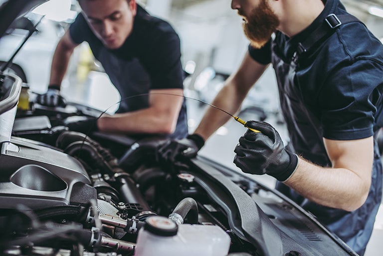 Two service technicians, one checking the oil level of an engine